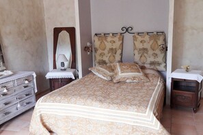 Ein Schlafzimmer mit einem Bett, einem Schminktisch, einem Nachttisch, einem Spiegel und Vorhängen.