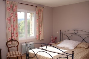 A bedroom with a bed, a chair, a radiator, and a window with curtains.