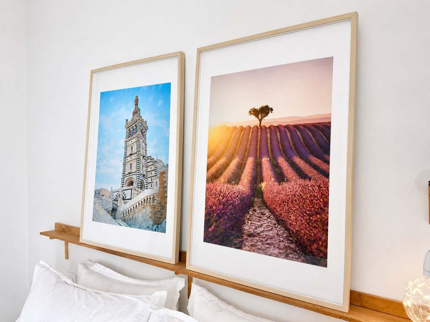 Twee ingekaderde foto's aan een muur, één toont een gebouw en de ander een veld met een boom.