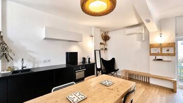 Une cuisine moderne avec un plan de travail noir, une table à manger en bois avec deux chaises, et un luminaire suspendu en fibres tressées.