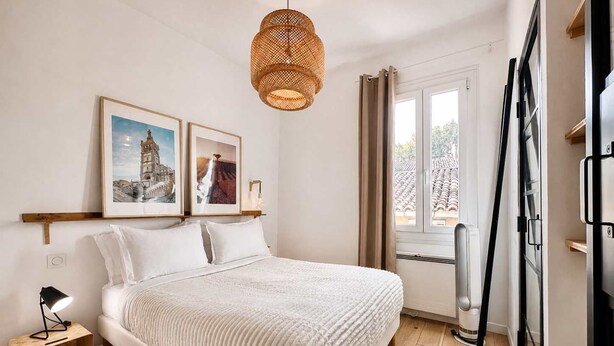 A bedroom with a bed, a bedside table with a lamp, a hanging rattan light fixture, and two framed pictures on the wall. - Ersextius, LMR2, Aix-en-Provence (Aix-en-Provence)