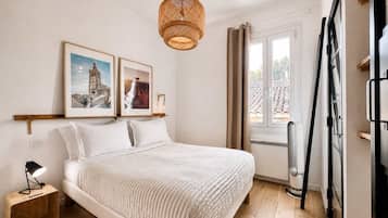 Une chambre à coucher avec un lit, une table de chevet avec une lampe, un luminaire suspendu en rotin et deux tableaux encadrés accrochés au mur.