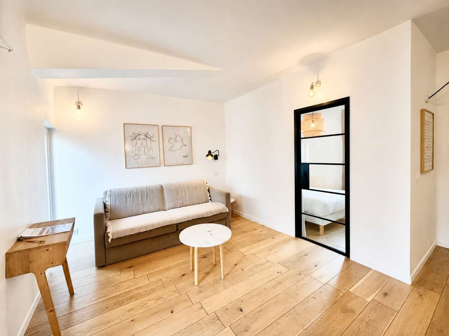 Een minimalistische woonkamer met een bank, een klein rond tafeltje en een boekenkast.