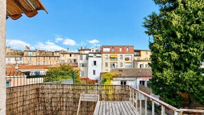A balcony with a wooden table and chairs, a bamboo fence, and a view of buildings. - Ersextius, LMR2, Aix-en-Provence (Aix-en-Provence)