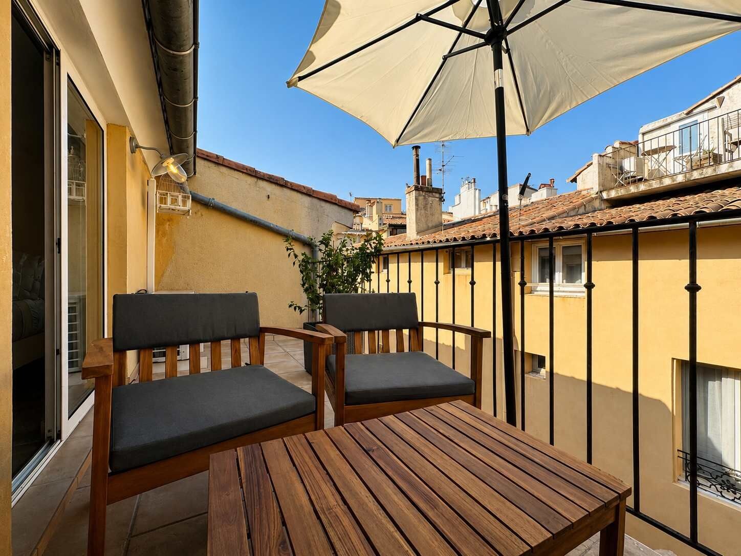 Ein Holztisch und zwei Stühle auf einem Balkon mit einem beigen Sonnenschirm.