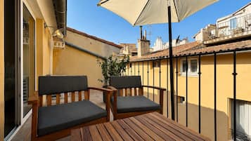Ein Holztisch und zwei Stühle auf einem Balkon mit einem beigen Sonnenschirm.