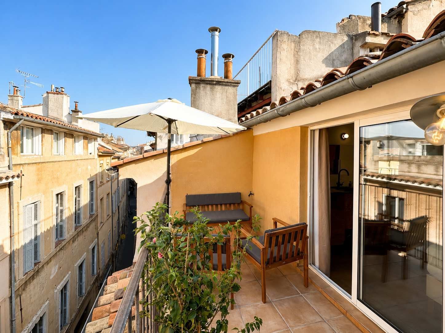 A balcony with a bench, a potted plant, and a view of adjacent buildings.