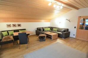 A cozy living room with a wooden ceiling, a sofa set with green cushions, a coffee table, and a small ottoman. - Holiday apartment in Krün with swimming pool (Krün)