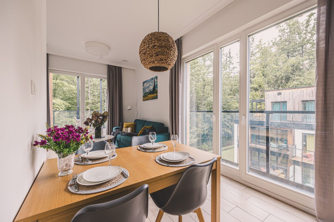 Un comedor con una mesa de madera dispuesta para cuatro, un florero y vistas al exterior a través de amplios ventanales.