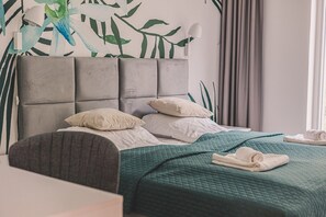 A hotel room with a bed, pillows, a headboard, a window with curtains, and a wall with a leafy pattern.
