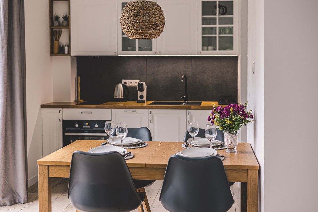 Una cocina moderna con armarios blancos, encimera de madera y una mesa de comedor para dos.