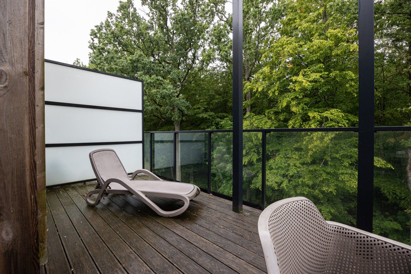 Ein Balkon mit Liegestuhl, Holzboden und Blick auf Bäume.