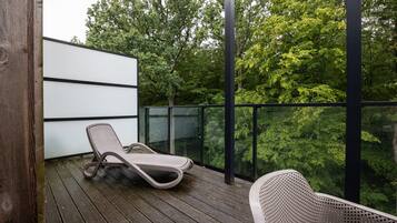 Ein Balkon mit Liegestuhl, Holzboden und Blick auf Bäume.