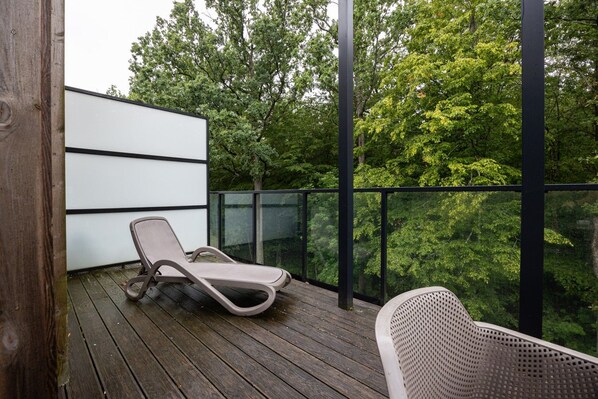 A balcony with a lounge chair, a wooden deck, and a view of trees.