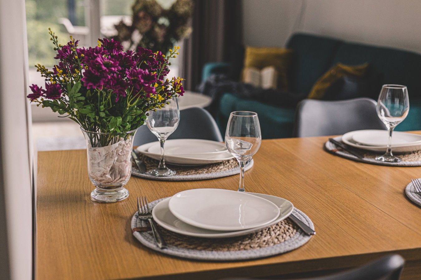 A dining table set with plates, cutlery, and glasses, with a vase of flowers on the left.