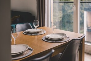 A dining table set with plates and wine glasses, positioned near a window with a view of greenery. - Lince Apartament | Z Dużym Tarasem w Koronach Drzew (Hajnówka)