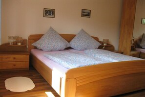 A bedroom with a wooden bed, two nightstands, a bedside table, a round rug, and two framed pictures on the wall. - Holiday apartment with 1 bedroom (Fischbachau\/Birkenstein)