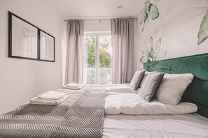 Ein Schlafzimmer mit einem Bett, einem grünen Kopfteil, einem Fenster mit Vorhängen und einer Wand mit einem Blattmuster.