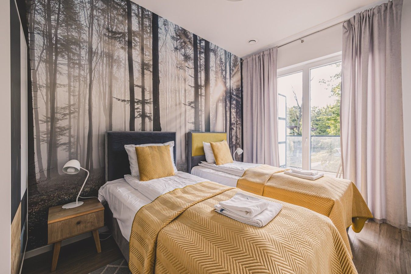 Habitación de hotel con dos camas, un ventanal grande y un mural temático de bosque.