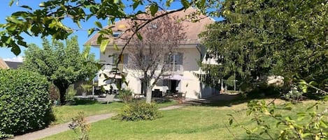 A residential property with a well-maintained lawn, a pathway leading to the house, and a variety of trees and shrubs.