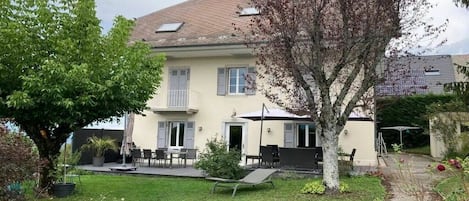 Une maison à deux étages dotée d’un patio, d’un espace salon extérieur et d’un chemin menant à l’entrée.