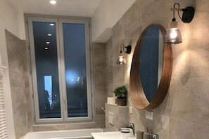 A modern bathroom with a large mirror, a bathtub, and a window. - Apartment with 1 bedroom (Aix les Bains)