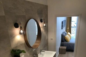 A bathroom with a large mirror, two wall-mounted lights, a sink, and a potted plant. - Apartment with 1 bedroom (Aix les Bains)