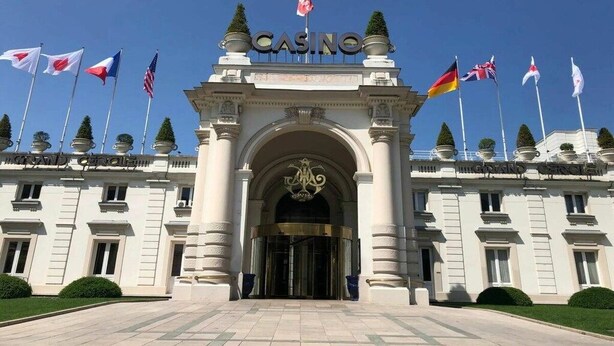 Una entrada imponent amb un rètol que diu 'CASINO', diverses banderes nacionals i un estil arquitectònic clàssic.