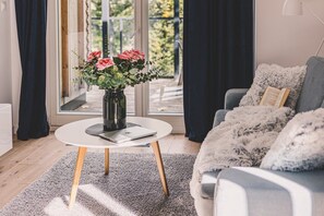 A modern living room with a round coffee table, a laptop, a vase with flowers, and a sofa with a fluffy throw.