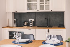 A modern kitchen with white cabinets, a black backsplash, and a wooden countertop. There is a coffee maker, a kettle, and a black faucet.