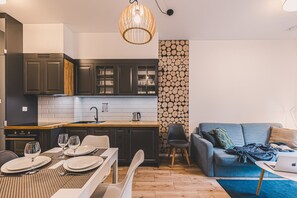 A modern kitchen with dark cabinets, a wooden countertop, and a hanging light fixture. - Castor Apartament  | Z Tarasem przy Puszczy (Hajnówka)