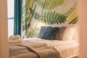 A bed with a patterned bedspread, pillows with geometric designs, and a wall with a leaf pattern.