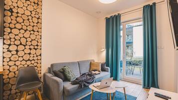 Een moderne woonkamer met een grijze bank, een klein rond tafeltje, een laptop en een televisie.