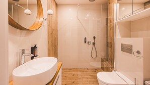 Une salle de bain moderne avec un grand lavabo ovale, des toilettes, une douche en verre et un mur d’accent en bois.