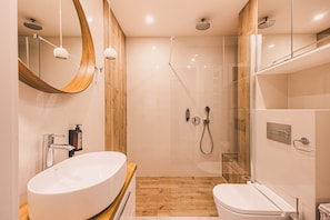 A modern bathroom with a large oval sink, a toilet, a glass-enclosed shower, and a wooden accent wall. - Castor Apartament  | Z Tarasem przy Puszczy (Hajnówka)