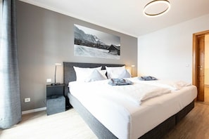 Quarto moderno com cama grande, cabeceira, mesas de cabeceira e um quadro na parede.