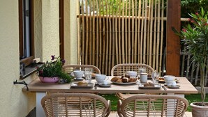 Een terras met rieten stoelen, een tafel gedekt met borden, bekers en een potplant.