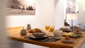 Een ontbijttafel met een theepot, kommen, glaasjes sinaasappelsap en een bord met plakjes komkommer.