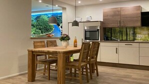 A modern kitchen with a dining area, wooden cabinets, and a large window with a scenic view. - Holiday apartment with 2 bedrooms (Merzig-Ballern)