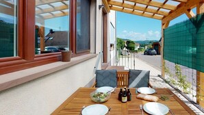 An outdoor dining area with a wooden table set for two, a bowl of salad, and bottles of beer. - Holiday apartment with 2 bedrooms (Merzig-Ballern)