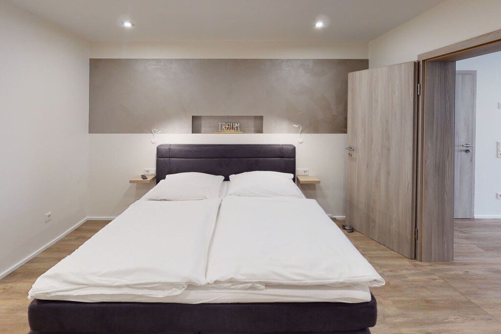 A double bed with a dark headboard, a bedside table, and a wall-mounted shelf with a sign above it.