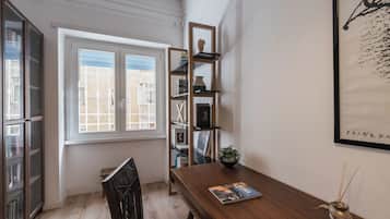 Ein Zimmer mit einem Holztisch, einem Bücherregal, einem Fenster mit Blick und einem gerahmten Kunstwerk an der Wand.