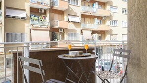 En balkong med ett bord och stolar, med utsikt över en bostadsbyggnad med flera balkonger och luftkonditioneringsaggregat.