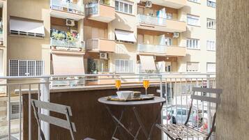 A balcony with a table and chairs, overlooking a residential building with multiple balconies and air conditioning units.