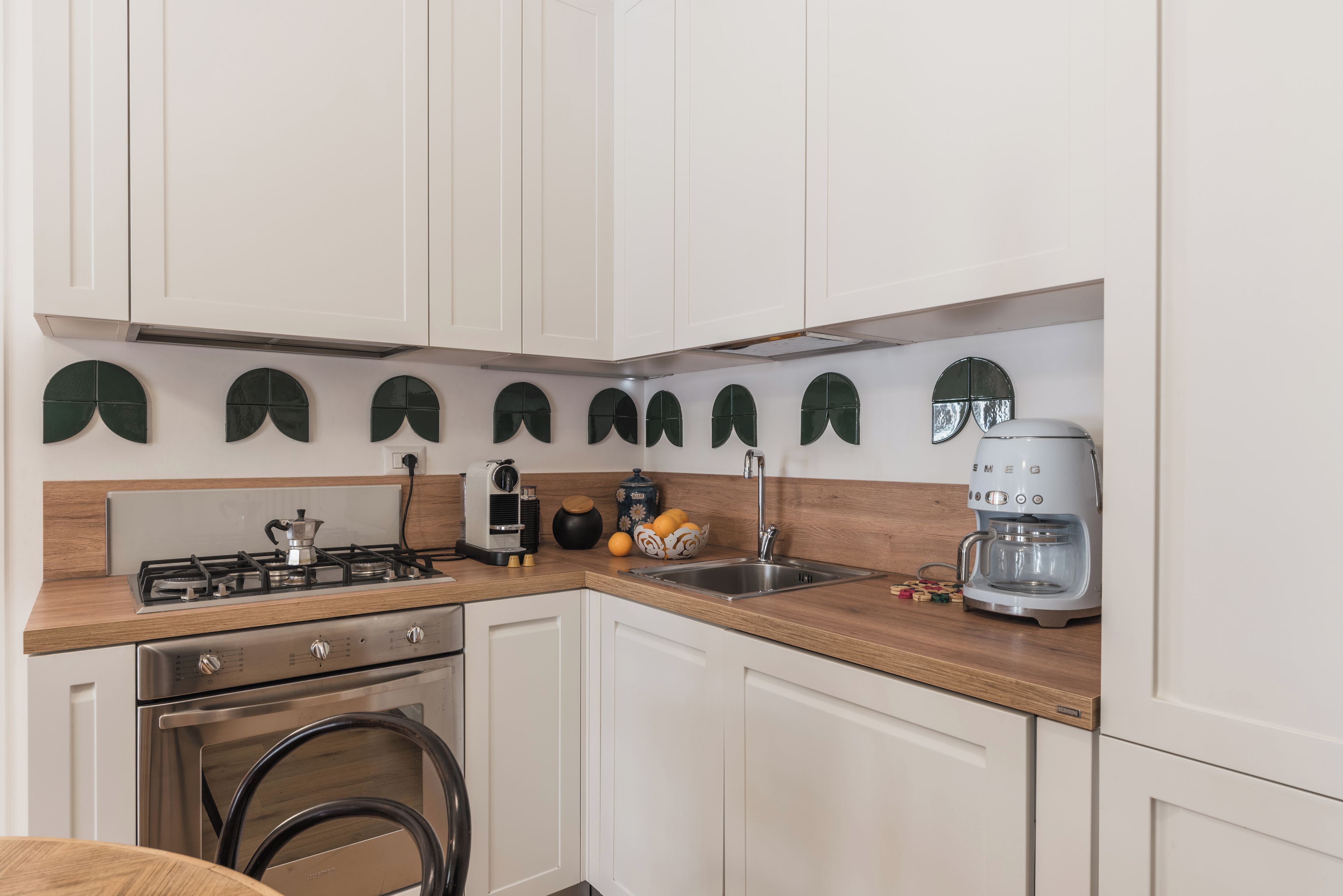 Une cuisine moderne avec des meubles blancs, une cuisinière à gaz, une machine à café et un évier.