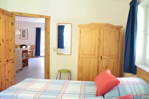 Ein Schlafzimmer mit einem Bett, einem Holzschrank, einem Spiegel und einem Fenster mit Vorhängen.