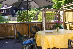Eine Terrasse im Freien mit einem Tisch, der mit einer gelben Tischdecke bedeckt ist, zwei Stühlen, einer Holz-Pergola und einem Holzzaun.