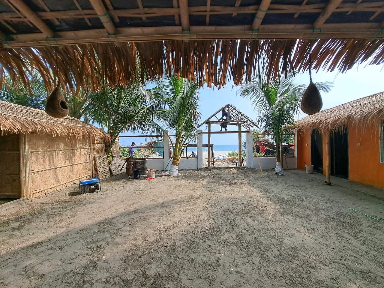 Une propriété située en bord de mer, avec des huttes à toits de chaume, une cour sablonneuse et un palmier.