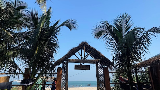 Ein Zugang zum Strand mit einer strohgedeckten Struktur, Palmen und freiem Blick auf das Meer.