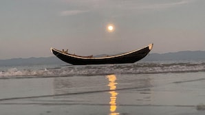 Ein Boot am Strand, Wellen und der Mond im Wasser.